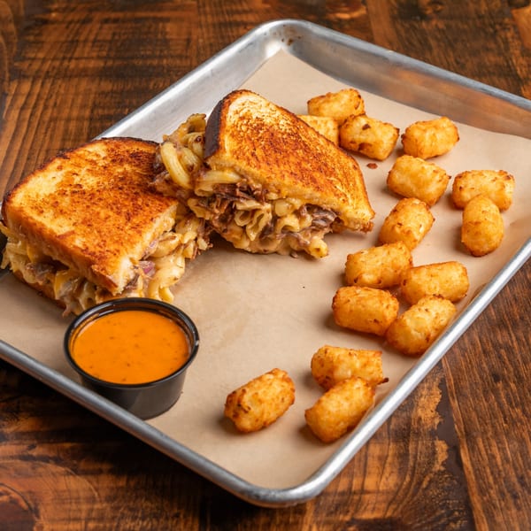 Grilled cheese sandwich with mac and cheese, beef, tater tots, and a side of dipping sauce.