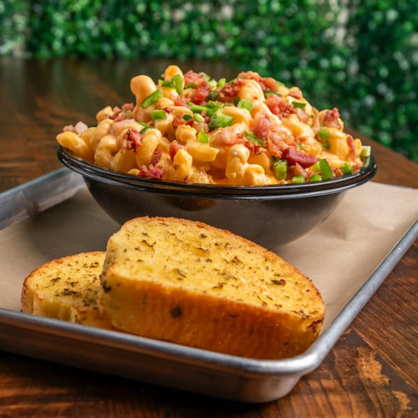 A black bowl of Mix & Mac Kitchen's mac and cheese with bacon and jalapeños, served with garlic bread.