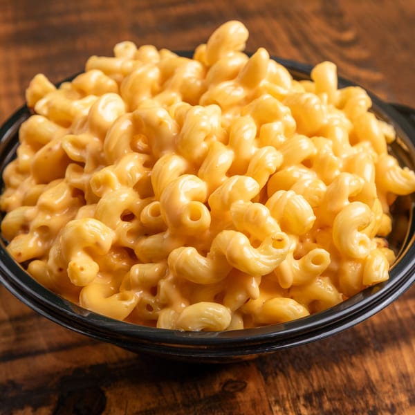 A close-up of a black bowl filled with creamy, golden macaroni and cheese on a wooden table.